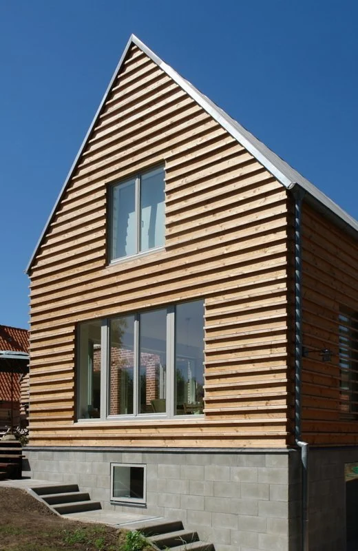 Holzverkleidetes Haus mit großen Fenstern und Satteldach unter blauem Himmel.