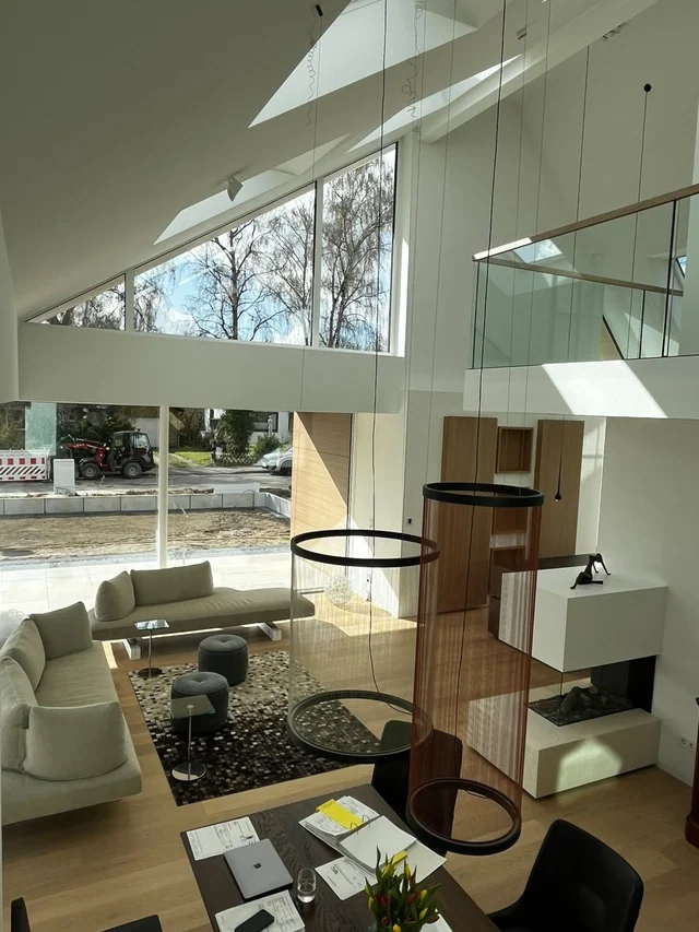 Modernes Wohnzimmer mit großen Fenstern, weißen Wänden, weißen Sofas, einem Teppich, einem kleinen Tisch, mehreren schwarzen Hockern, einer Steinkamin, einer Holzverkleidung und Designleuchten.